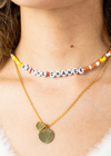 Women wearing a beaded chocker that Be The Change layered with a gold necklace with a circle and heart charm.